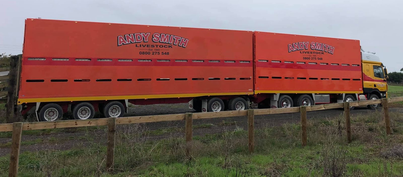 Side view of a full Andy Smith Livestock truck and trailer alongside a farm fence