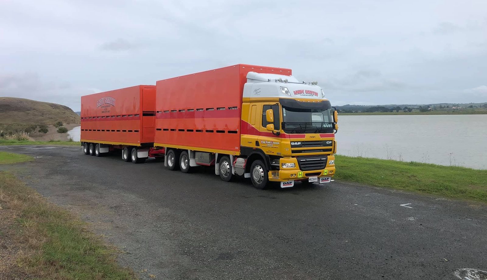 Andy Smith Livestock truck and trailer with red stock crates parked beside a lake